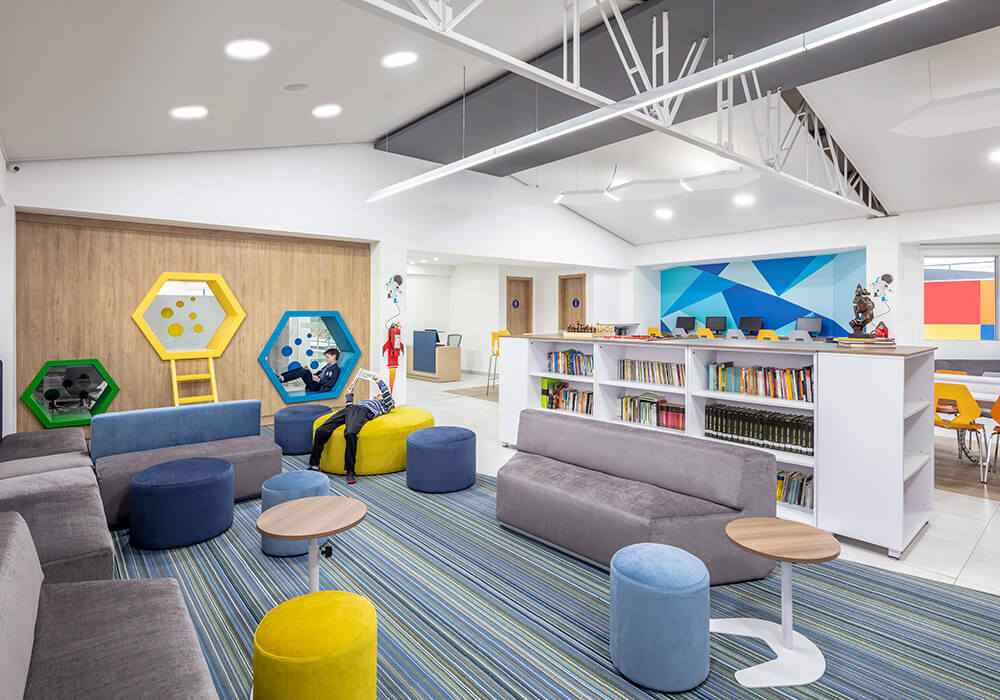 Zona de colaboración en Colegio Intisana diseñada por Mepal Carvajal Espacios con mesas largas, sillas coloridas y estanterías móviles